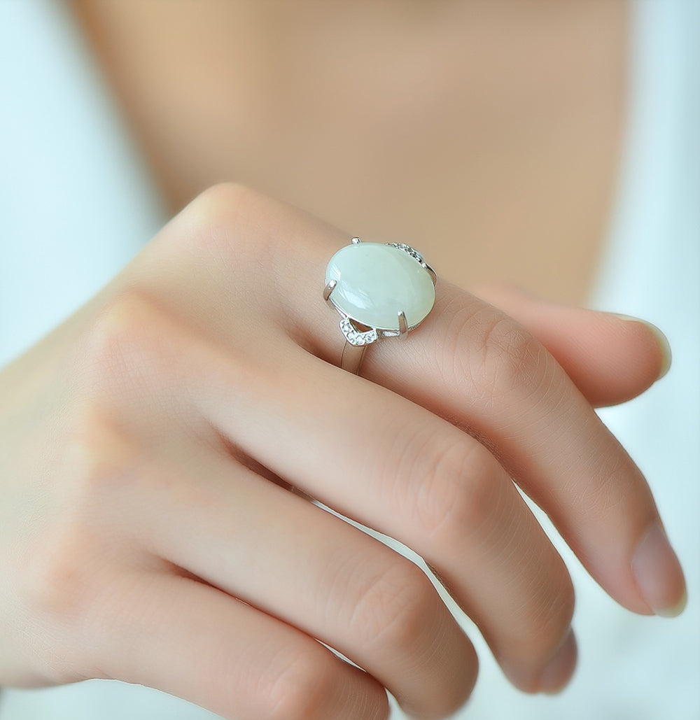 White jade oval cabochon ring with four prongs in 925 sterling silver; simple yet elegant design with rhomboid zircon stones on both sides.
