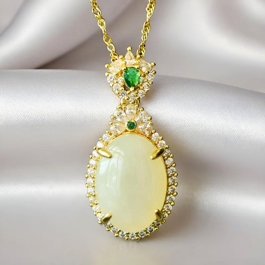An oval Hetian jade main stone, topped with a golden floral crown, and adorned with emerald green gemstones; a pendant necklace.