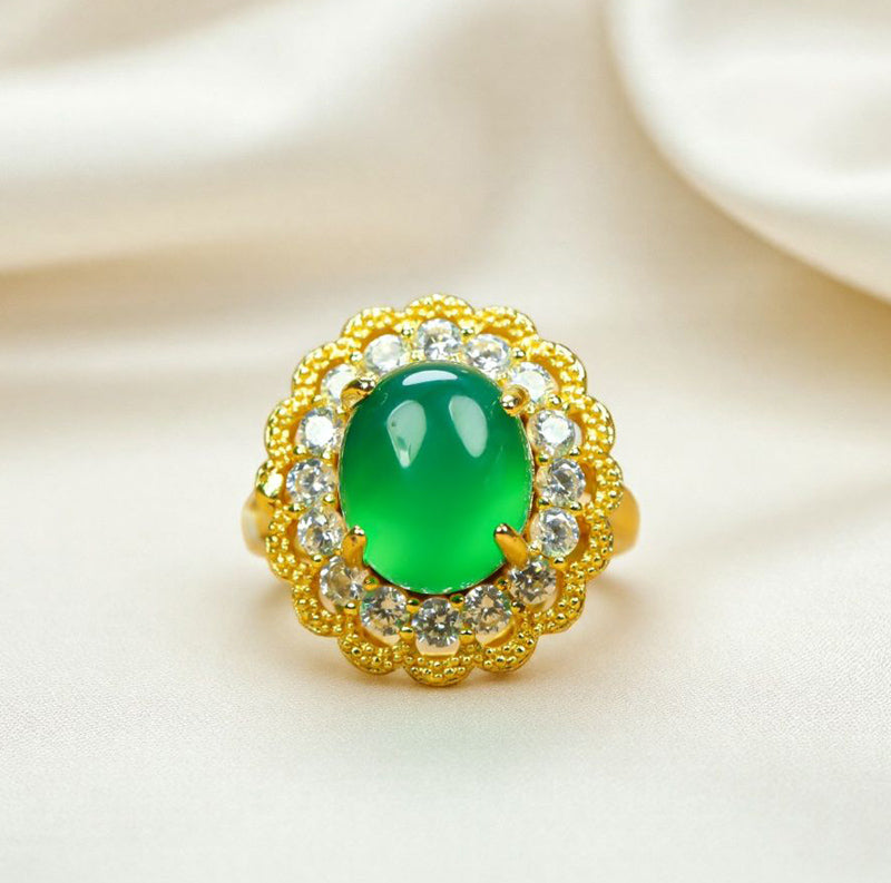 Emerald-green jade cabochon ring featuring a golden flower design; the golden petal-shaped setting is accented with inlaid zircon stones.