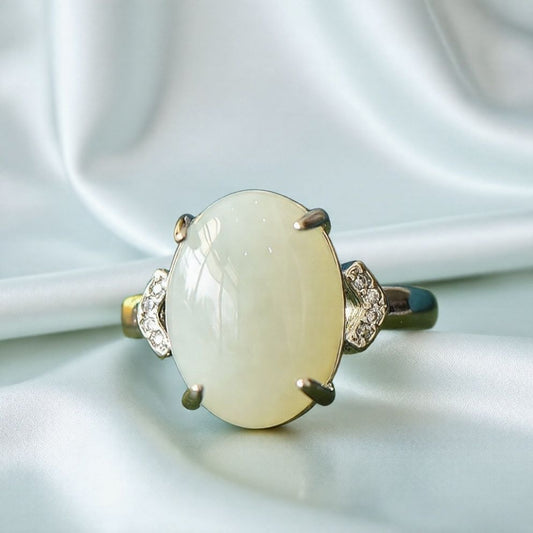 White jade oval cabochon ring with four prongs in 925 sterling silver; simple yet elegant design with rhomboid zircon stones on both sides.
