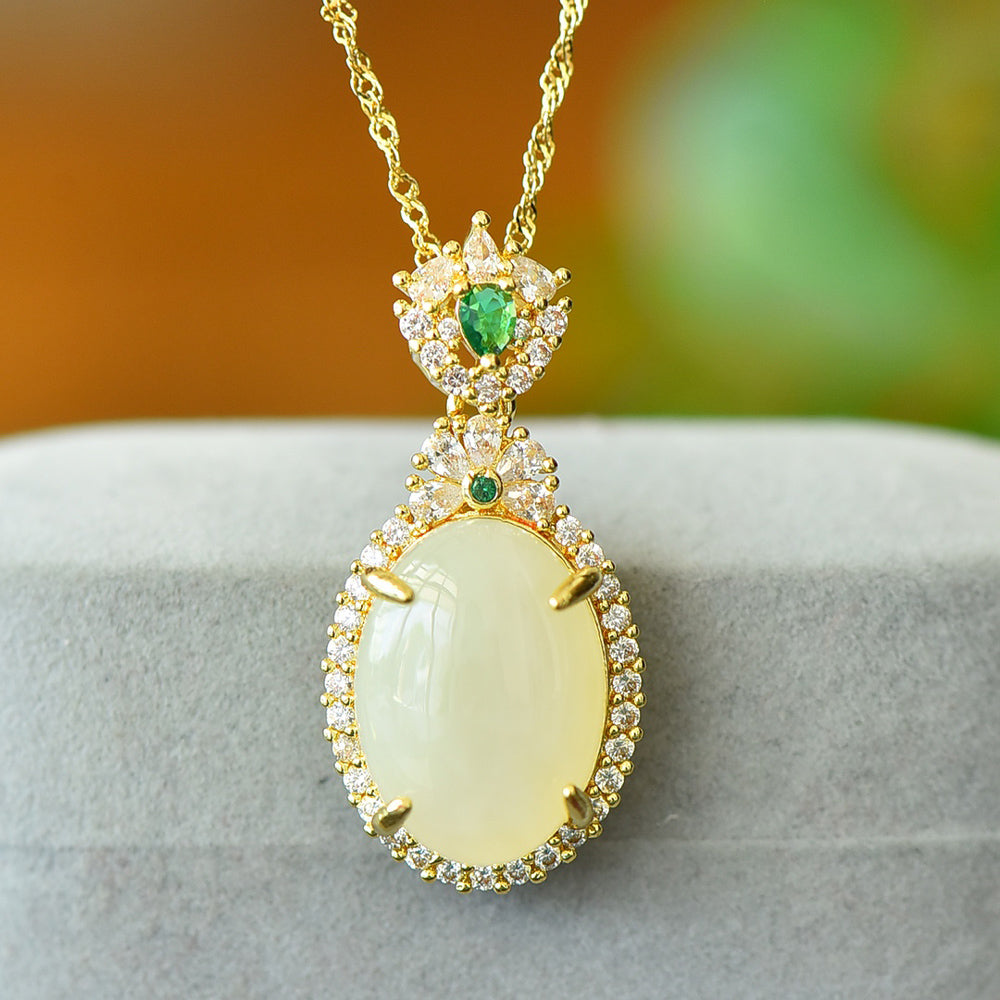 An oval Hetian jade main stone, topped with a golden floral crown, and adorned with emerald green gemstones; a pendant necklace.