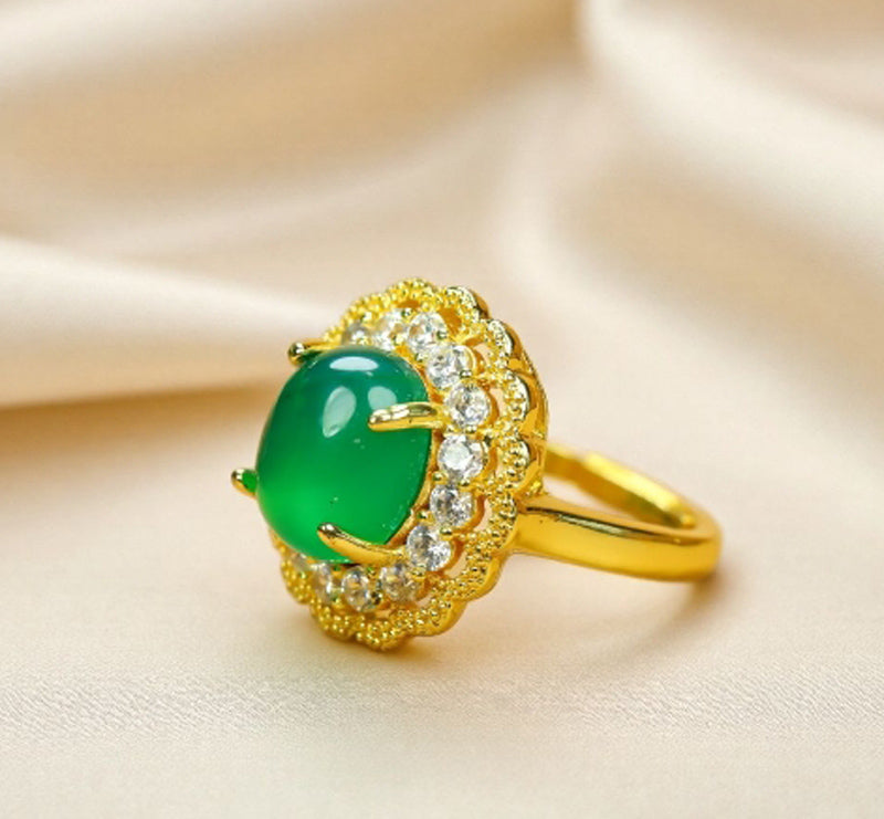 Emerald-green jade cabochon ring featuring a golden flower design; the golden petal-shaped setting is accented with inlaid zircon stones.