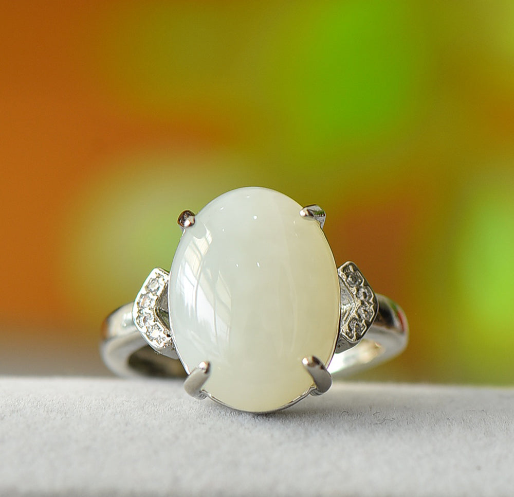 White jade oval cabochon ring with four prongs in 925 sterling silver; simple yet elegant design with rhomboid zircon stones on both sides.