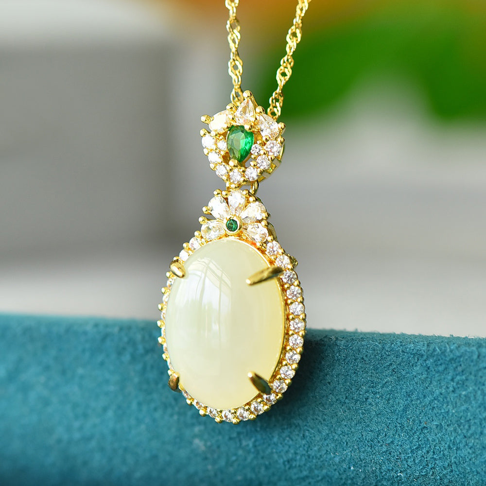 An oval Hetian jade main stone, topped with a golden floral crown, and adorned with emerald green gemstones; a pendant necklace.