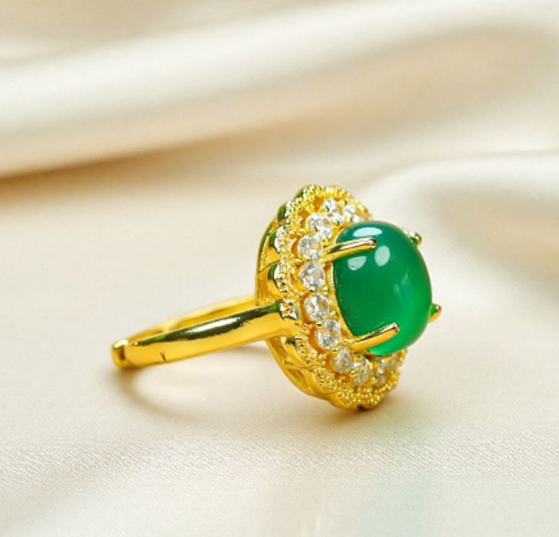 Emerald-green jade cabochon ring featuring a golden flower design; the golden petal-shaped setting is accented with inlaid zircon stones.