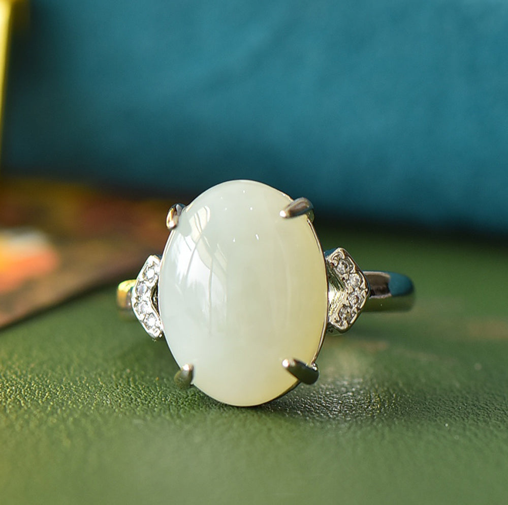 White jade oval cabochon ring with four prongs in 925 sterling silver; simple yet elegant design with rhomboid zircon stones on both sides.