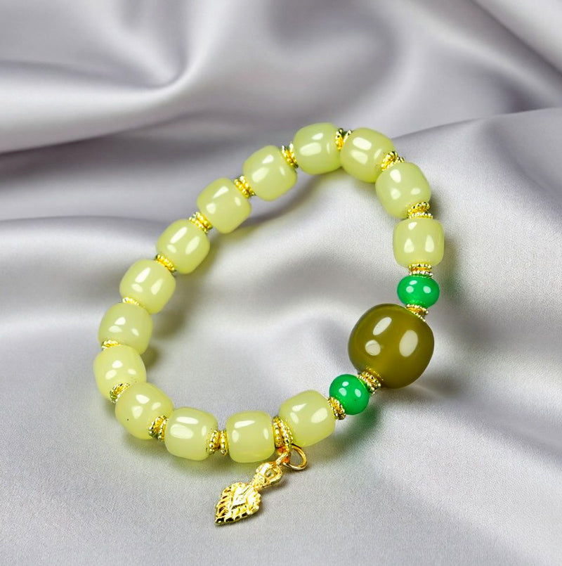 Yellow-green chalcedony barrel bead bracelet featuring gold spacers, a deep olive-green main bead, emerald-green small round beads, and a gold lotus-shaped charm.