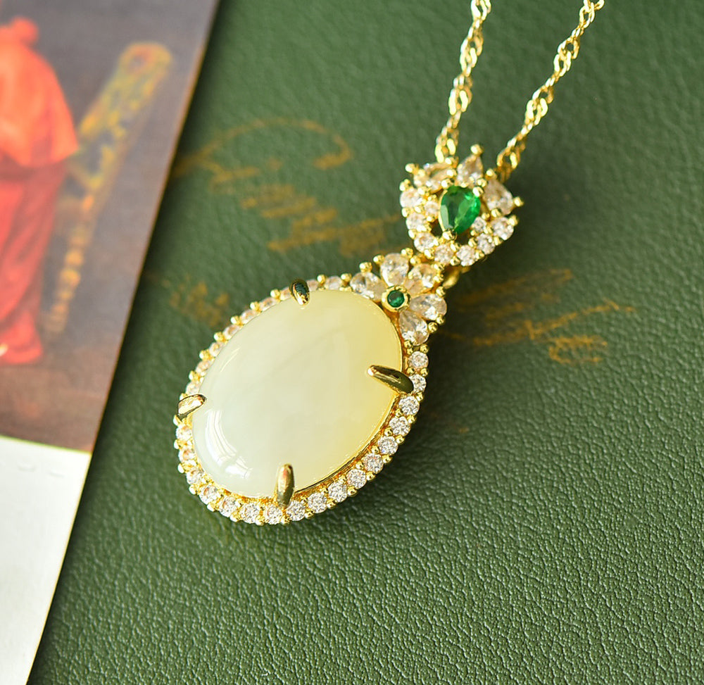 An oval Hetian jade main stone, topped with a golden floral crown, and adorned with emerald green gemstones; a pendant necklace.