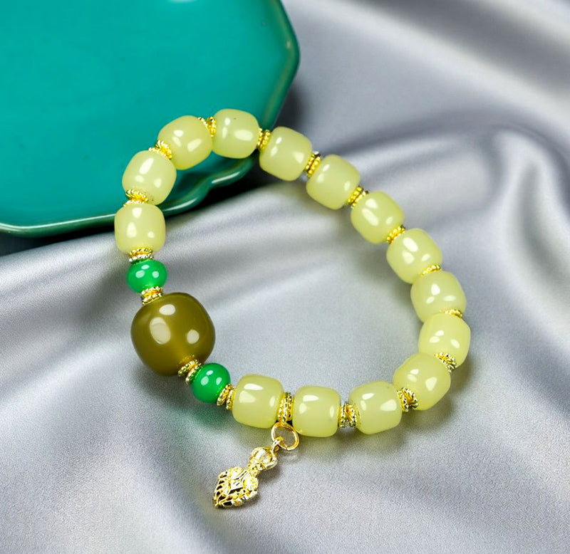 Yellow-green chalcedony barrel bead bracelet featuring gold spacers, a deep olive-green main bead, emerald-green small round beads, and a gold lotus-shaped charm.