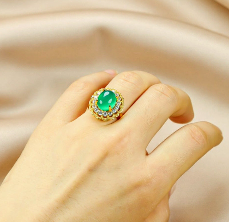 Emerald-green jade cabochon ring featuring a golden flower design; the golden petal-shaped setting is accented with inlaid zircon stones.