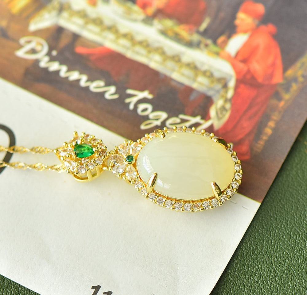 An oval Hetian jade main stone, topped with a golden floral crown, and adorned with emerald green gemstones; a pendant necklace.