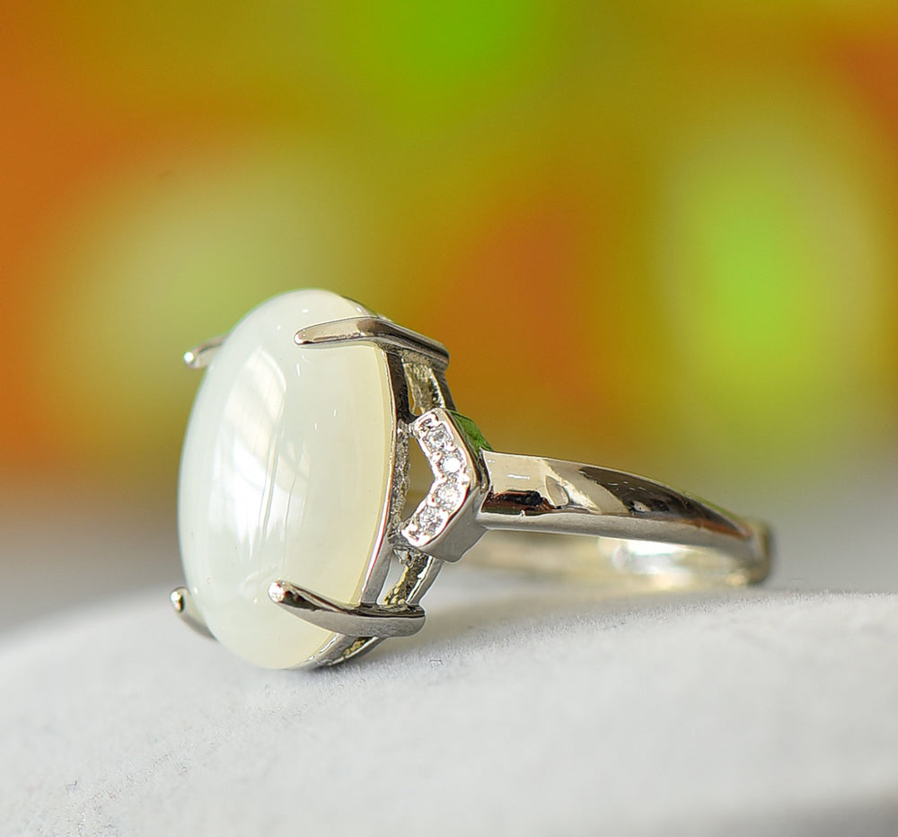 White jade oval cabochon ring with four prongs in 925 sterling silver; simple yet elegant design with rhomboid zircon stones on both sides.