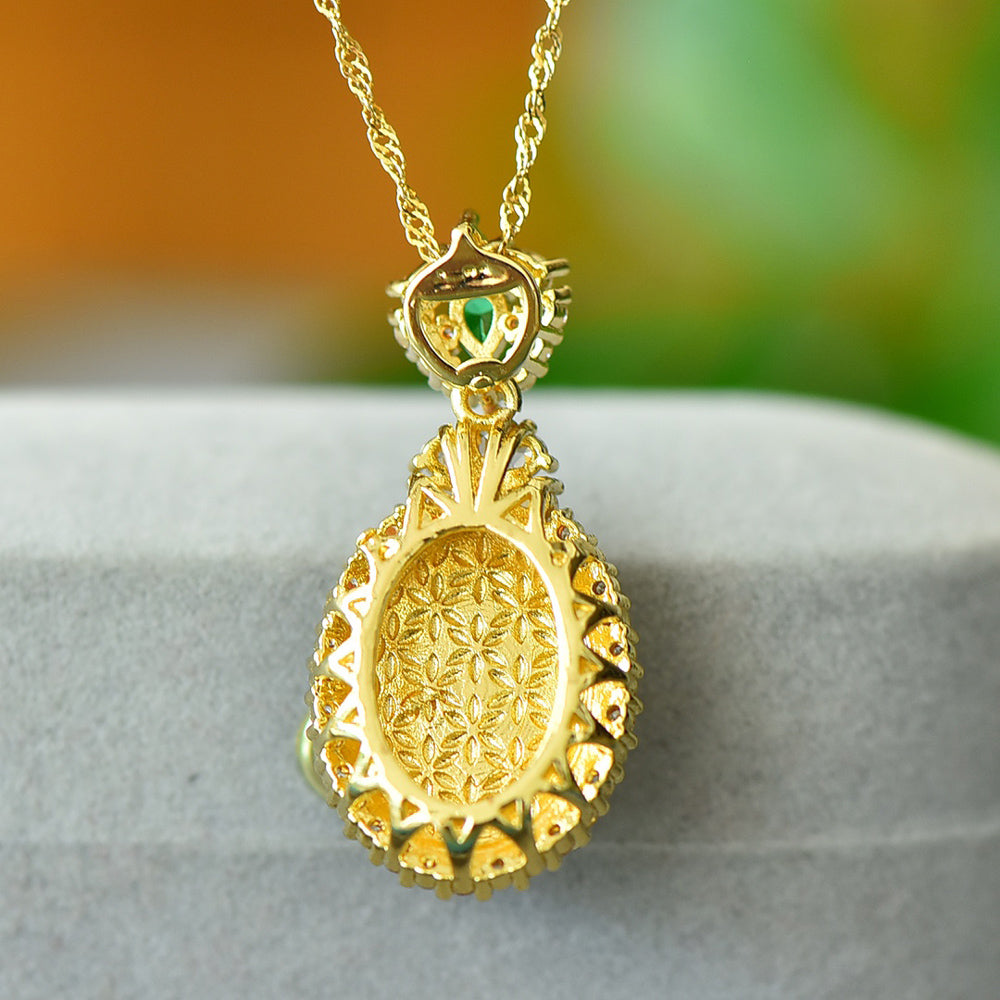 An oval Hetian jade main stone, topped with a golden floral crown, and adorned with emerald green gemstones; a pendant necklace.