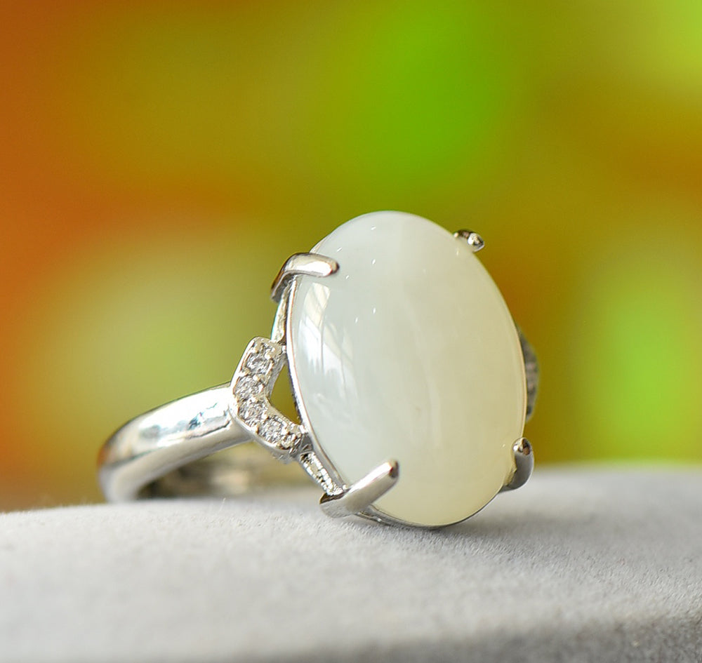 White jade oval cabochon ring with four prongs in 925 sterling silver; simple yet elegant design with rhomboid zircon stones on both sides.