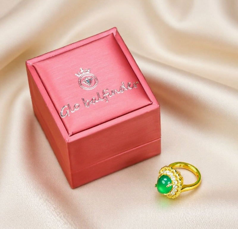 Emerald-green jade cabochon ring featuring a golden flower design; the golden petal-shaped setting is accented with inlaid zircon stones.