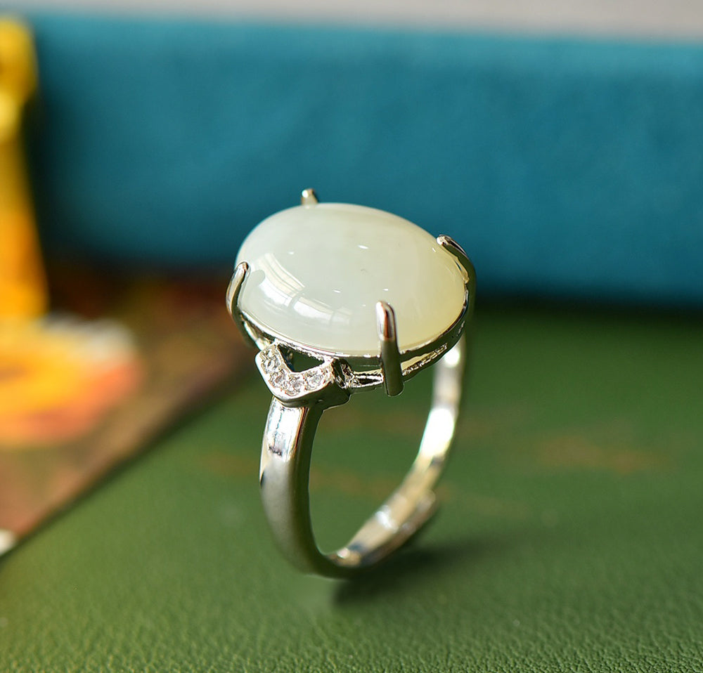 White jade oval cabochon ring with four prongs in 925 sterling silver; simple yet elegant design with rhomboid zircon stones on both sides.